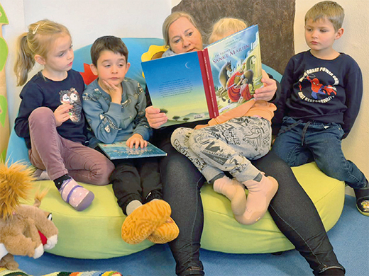 Lieblingsorte Vier Kinder sitzen auf einer grünen Sitzbank, eine Person liest ihnen aus einem Buch vor